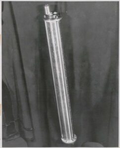 A mercury delay line memory tank for the UNIVAC computer, photographed against a dark background, circa 1951. The cylindrical aluminum tube is approximately two feet long with crystal transducers at each end. Eckert-Mauchly Computer Corporation.
